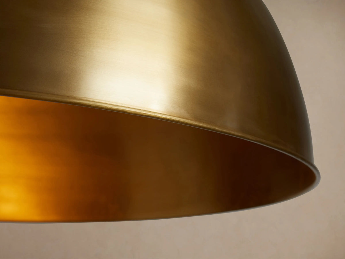 Watley Dome Pendant: A large, smooth, antique brass dome-shaped light fixture hanging from a slender rod against a neutral background.
