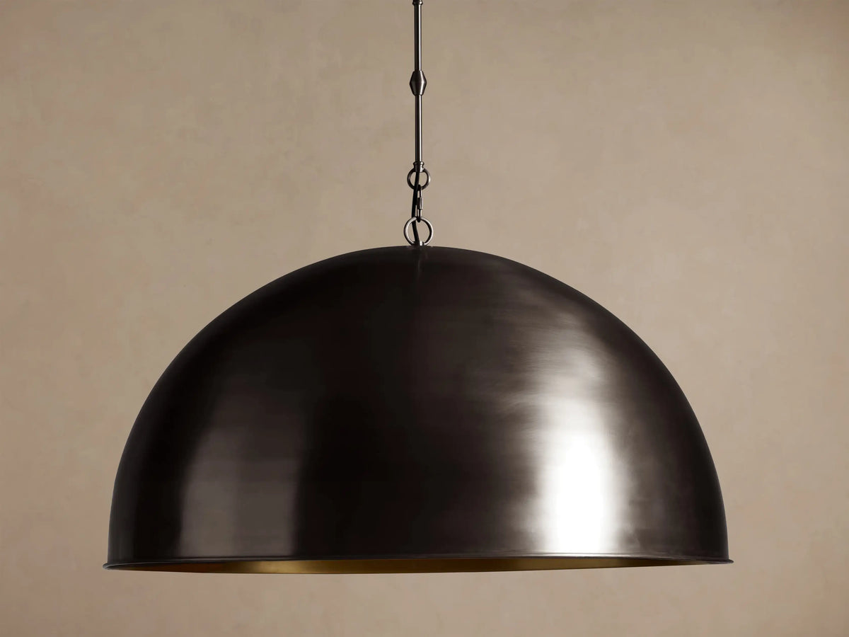 Watley Dome Pendant. Dark oxidized brass dome light, showing a gleaming golden interior, hanging against a brown wall.