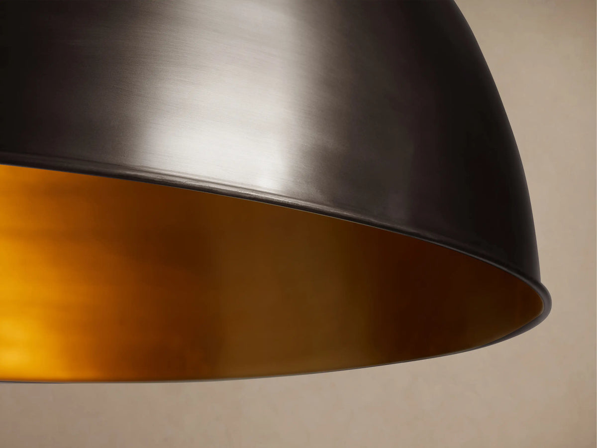 Watley Dome Pendant, a dark metallic dome light fixture showing a polished brass interior, suspended by a dark chain.