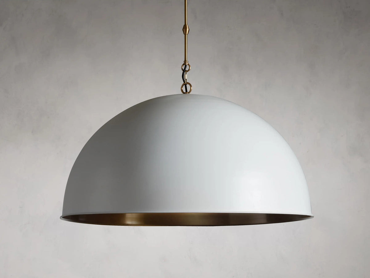 Dome-shaped pendant light with white exterior, brass interior, and brass chain. Elegant minimalist design against gray background.