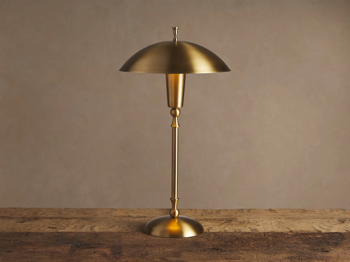 Archard Table Lamp with a lustrous brass finish, domed shade, and slender stem, standing on a rustic wooden surface.