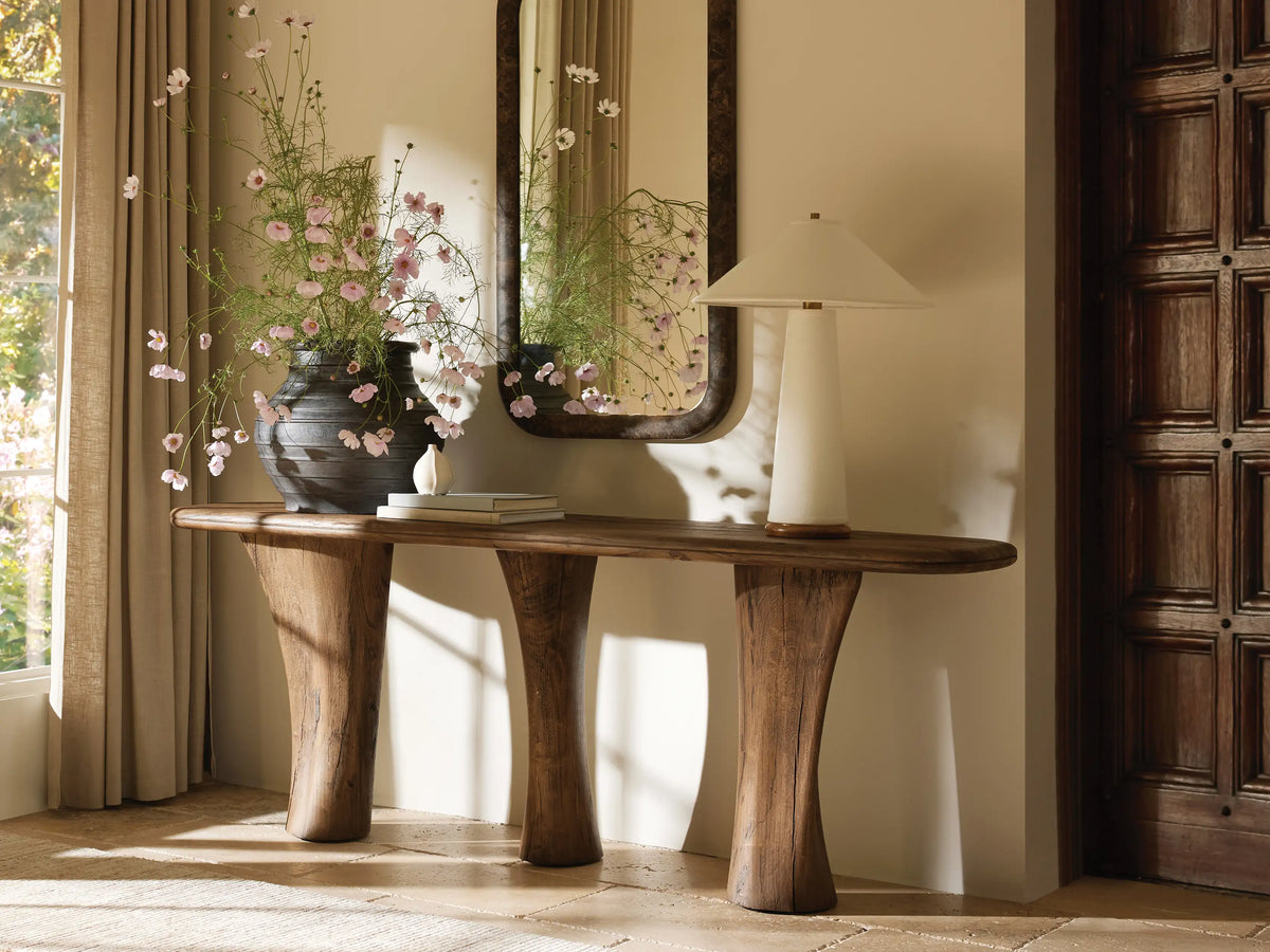 Ombra Table Lamp: Tapered natural linen shade & cylindrical linen base on a round teak wood bottom with brass accent. Lit, on wood.