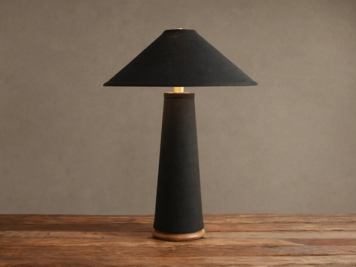 Ombra Table Lamp: Dark linen conical base & shade, teak wood base, antiqued brass accent, on rustic wood table.