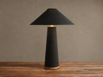Ombra Table Lamp: Dark linen conical base & shade, teak wood base, antiqued brass accent, on rustic wood table.