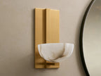 Belmira Sconce: Brass-finished wall light with glowing, bowl-shaped alabaster shade on a textured wall next to a mirror.