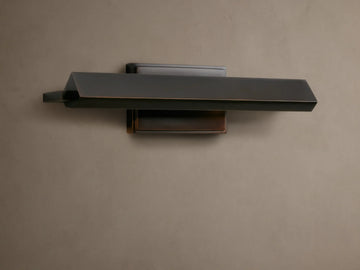 Zaeden Picture Light, dark bronze-plated with a horizontal angled bar and rectangular backplate, mounted on a textured brown wall.
