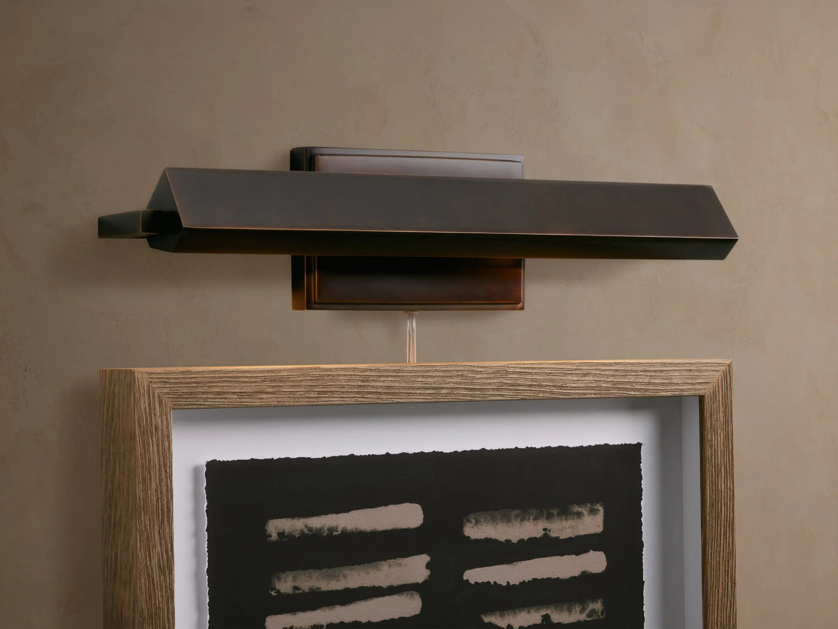 Zaeden Picture Light, angled dark bronze-plated iron fixture, mounted horizontally against a textured beige wall.