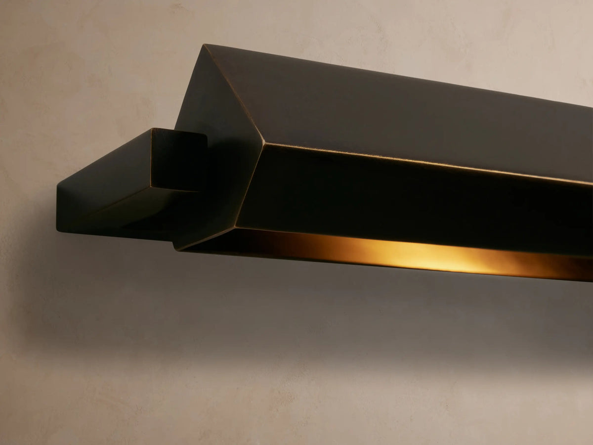 Horizontal Zaeden Picture Light with bronze-plated finish, featuring an angled bar design, mounted on a textured beige wall.