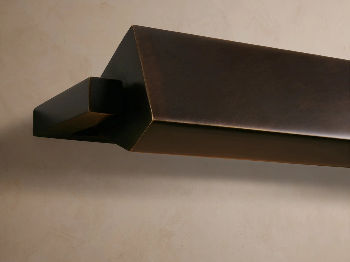 Zaeden Picture Light, bronze-plated iron with geometric design, mounted on a neutral wall, emitting warm light downwards.