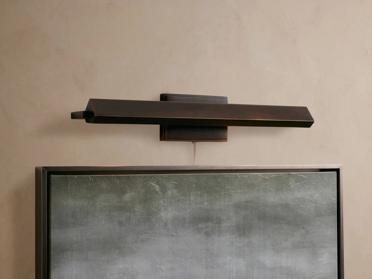 Close-up of a bronze-plated Zaeden Picture Light with an angular, geometric design mounted on a textured beige wall.