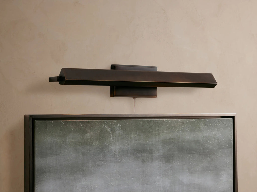Close-up of a bronze-plated Zaeden Picture Light with an angular, geometric design mounted on a textured beige wall.