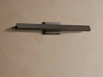 Zaeden Picture Light, horizontal bronze-plated iron fixture mounted on a light beige wall. It has a rectangular bar with an angled front.
