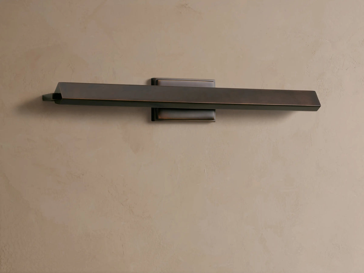 Zaeden Picture Light: horizontal dark bronze iron fixture with a flat bar & angled end, centered on a light beige textured wall.