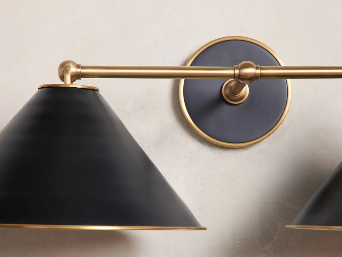 Matte black and brass Arno Double Sconce with conical shades and polished brass interior, mounted on a white wall.