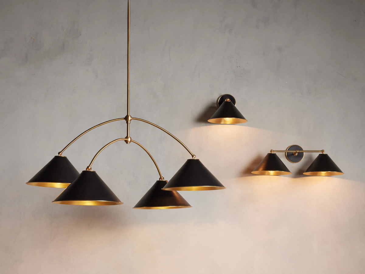 Arno Double Sconce in matte black with polished brass accents, featuring conical shades and circular backplate on a neutral wall.