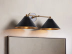 Black Arno Double Sconce with polished brass interior, mounted on wall, casting warm light. Accompanied by a matching chandelier.