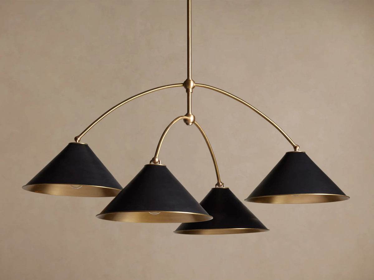 Arno Round Chandelier with a gold brass frame and four matte black conical shades, each with a polished brass interior, hanging.
