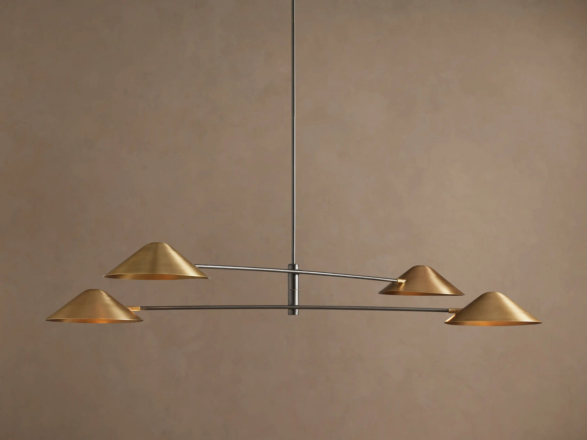 Simms Chandelier with four conical polished brass shades facing down, mounted on dark horizontal arms against a brown wall.