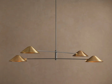 Simms Chandelier with four conical polished brass shades facing down, mounted on dark horizontal arms against a brown wall.