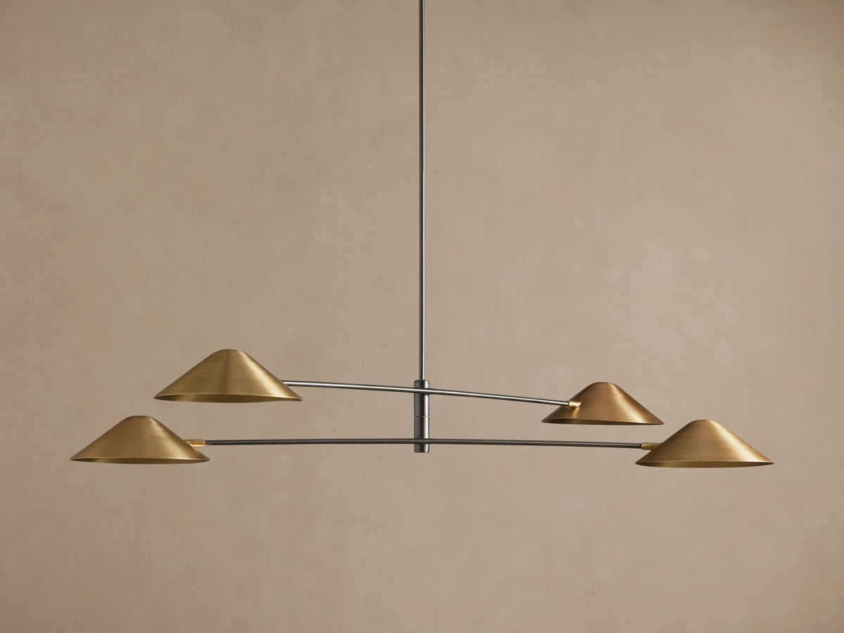 Simms Chandelier with four conical polished brass shades facing down, mounted on dark horizontal arms against a brown wall.