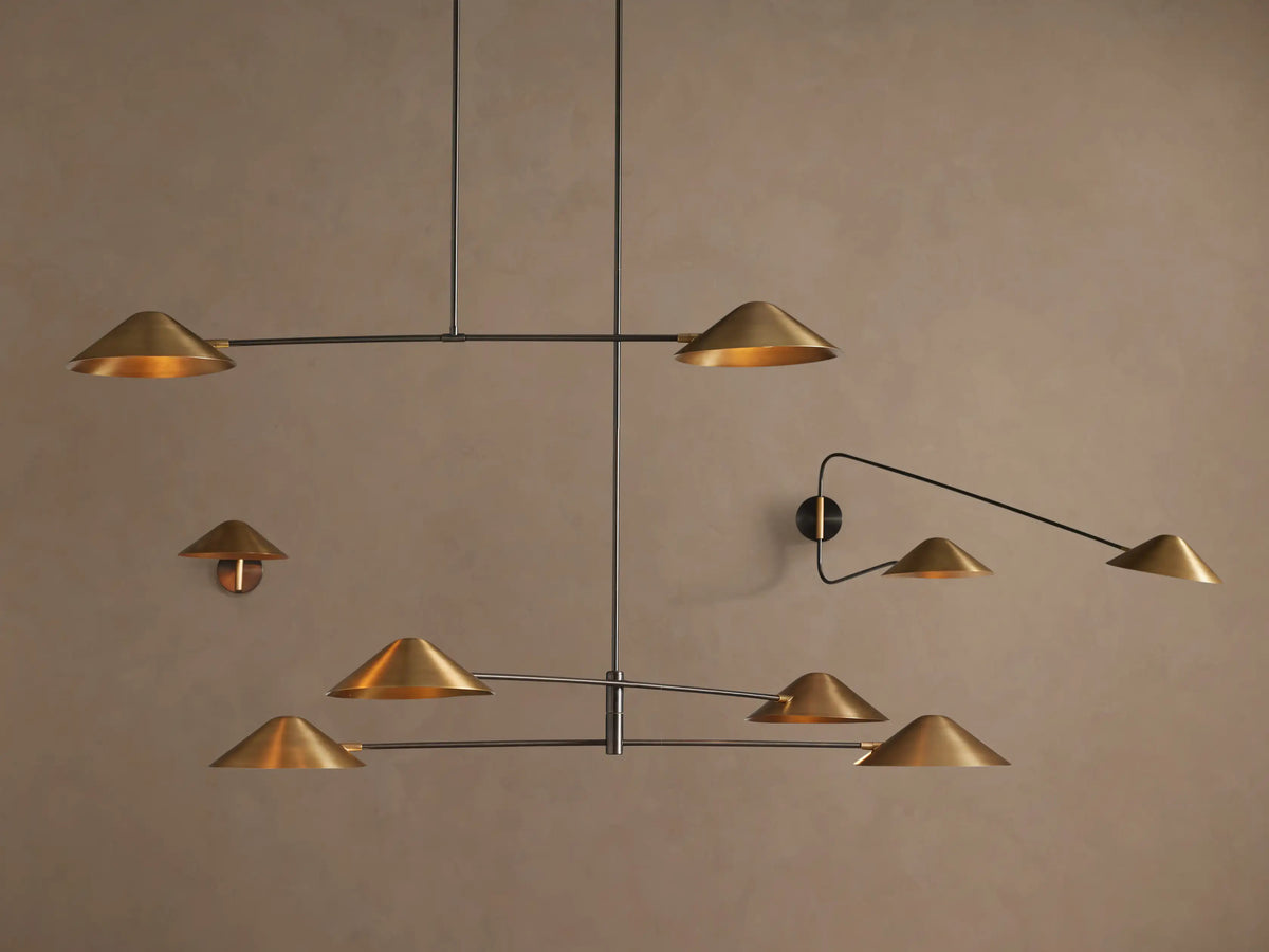 Simms Chandelier: Modern oxidized brass chandelier with four conical shades pointing outwards on linear silver arms, against a taupe wall.