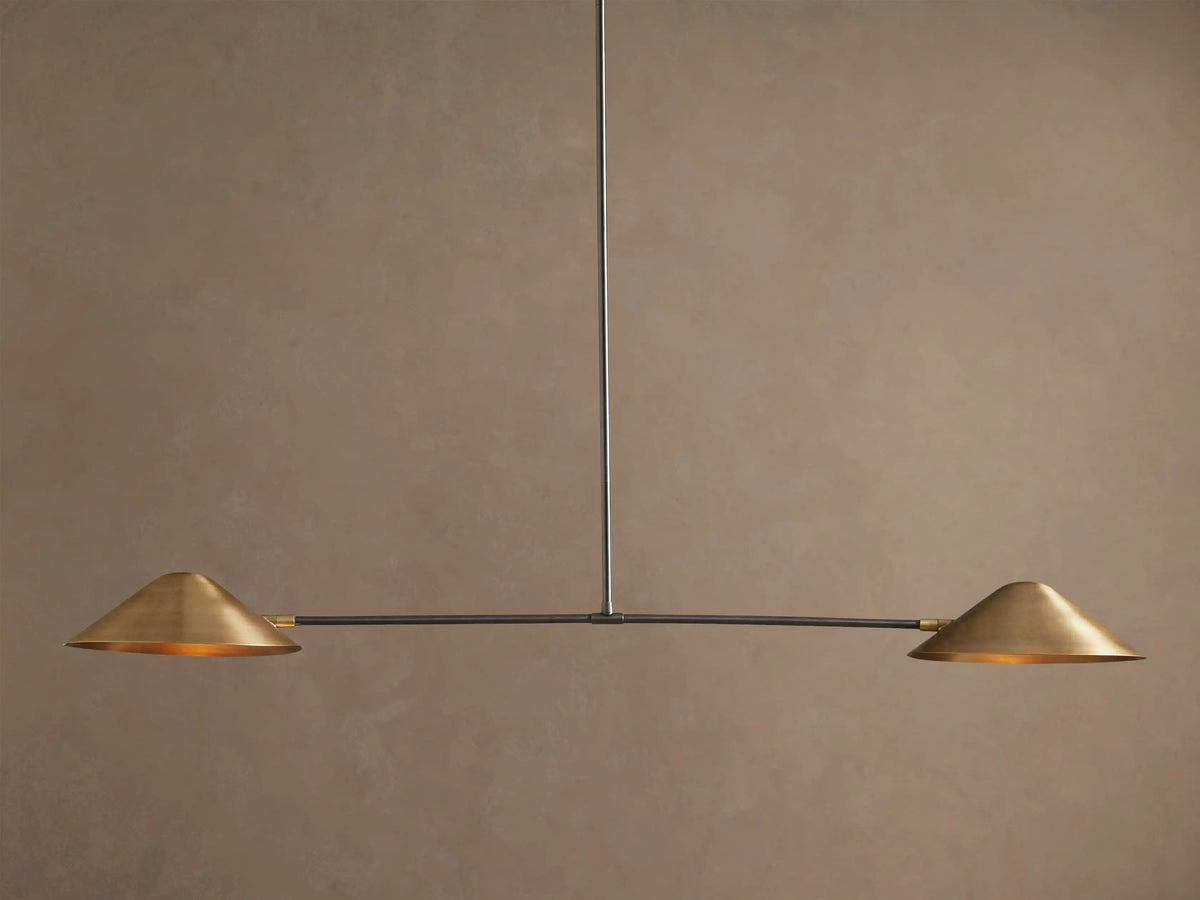 Simms Linear Chandelier with two downward-facing brass conical shades on a dark horizontal bar, suspended against a taupe wall.