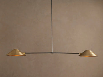 Simms Linear Chandelier with two downward-facing brass conical shades on a dark horizontal bar, suspended against a taupe wall.