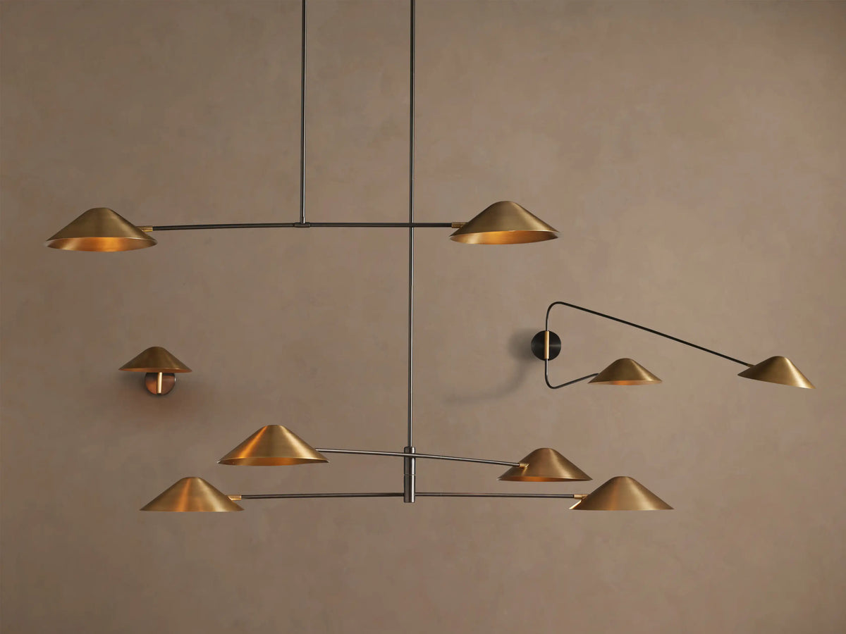 Simms Linear Chandelier. Modern fixture with two conical polished brass shades on a dark linear bar, suspended against a tan wall.