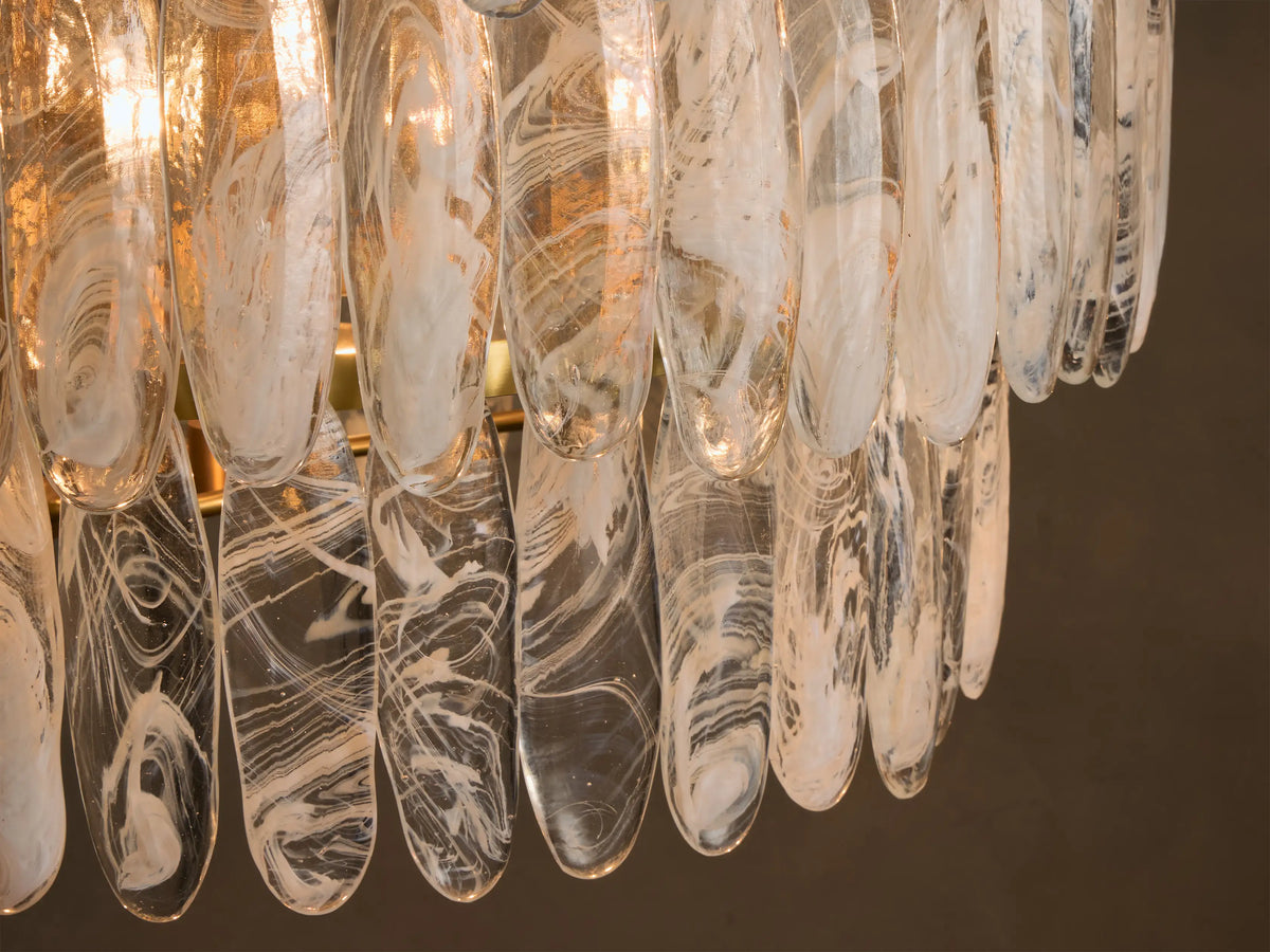 Front view of a three-tiered chandelier featuring oval clear glass panels with white swirled patterns, illuminated by warm lights.