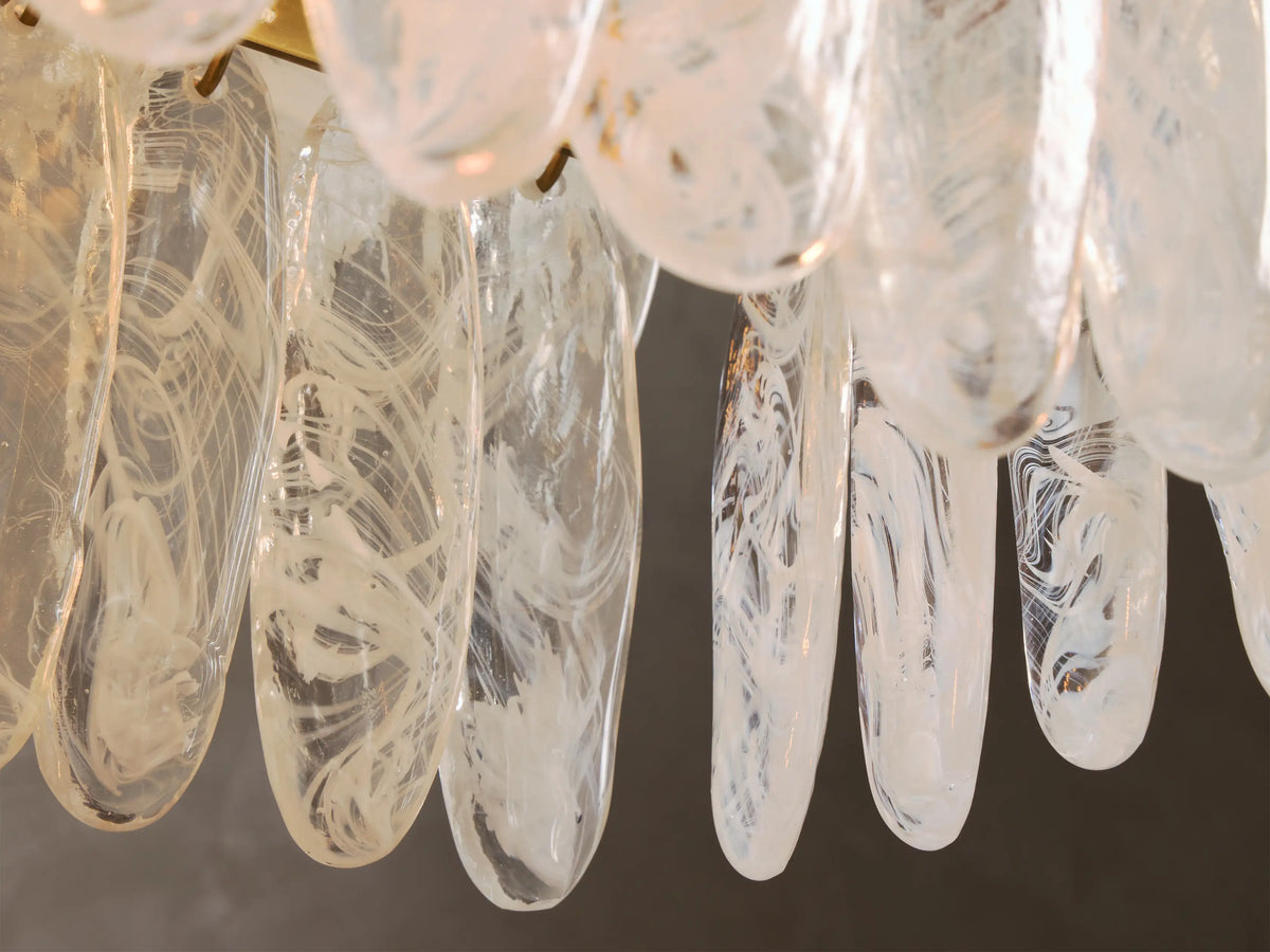 Close-up of clear glass art pieces with internal white swirled patterns, elongated and hanging vertically.