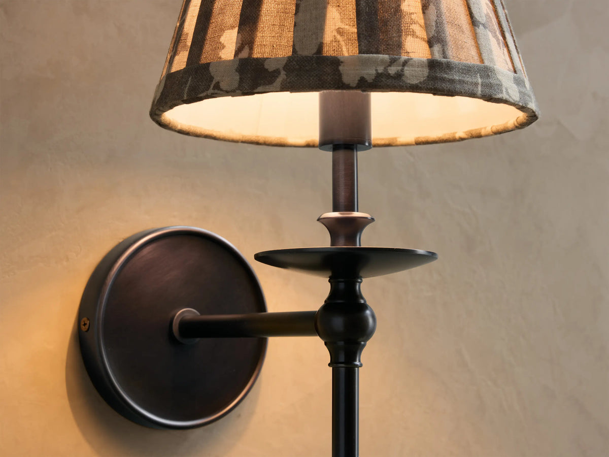 Front view of Winslow Single Sconce with dark bronze finish and pleated botanical fabric shade, mounted on a wall next to a mirror.