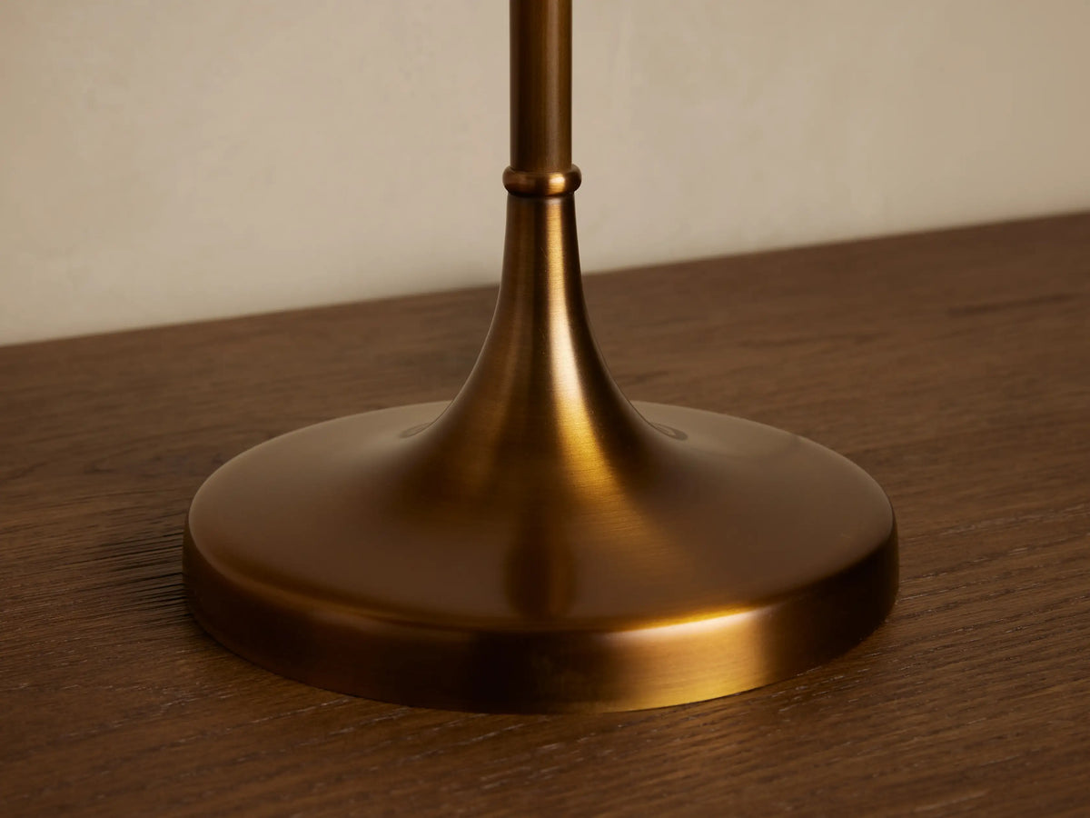 Lorelei Table Lamp, antique brass base & tall white linen shade, on wood, against a beige wall, with decor.
