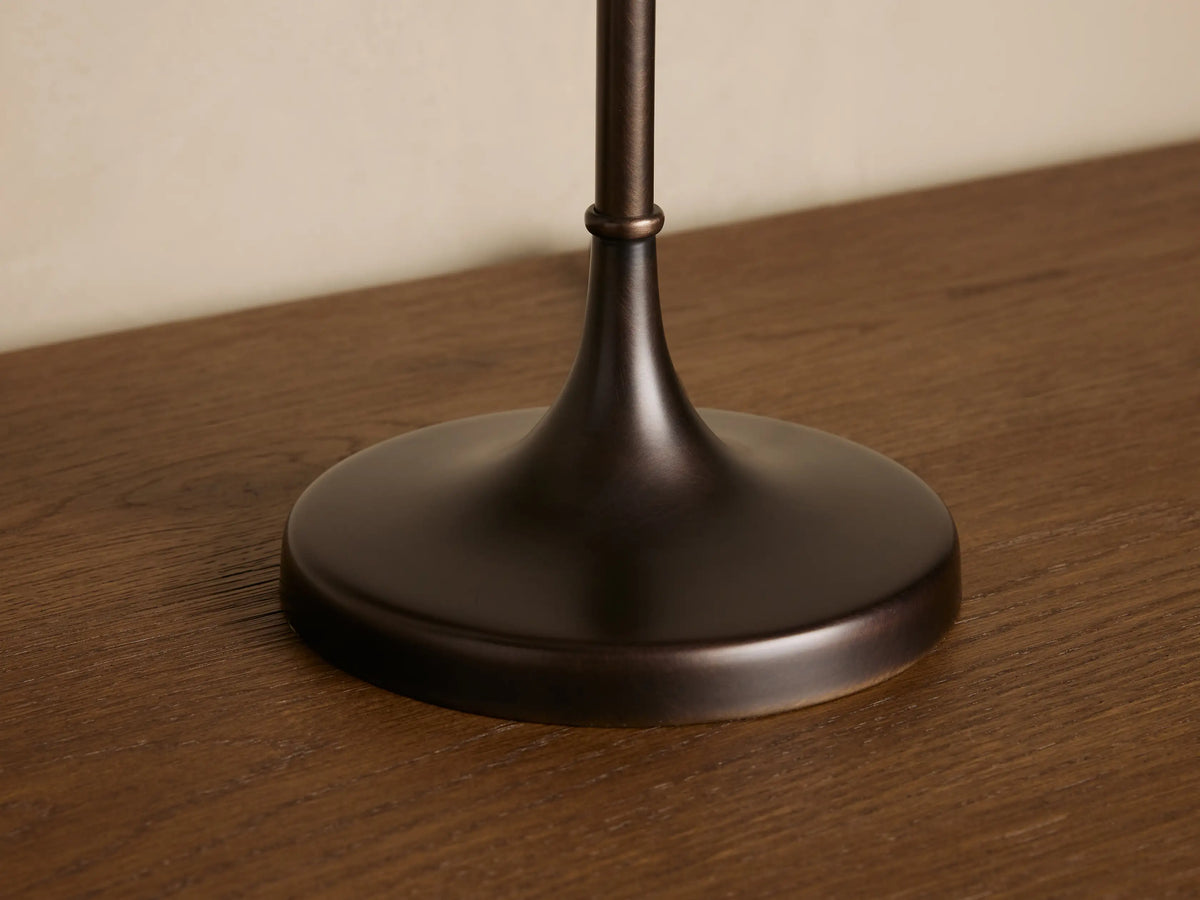 Lorelei Table Lamp with bronze base, thin stem, and cylindrical flax linen shade on a wooden surface with a small vase.