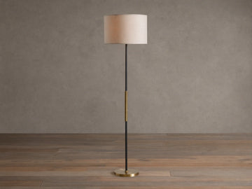 Ardea Floor Lamp with a matte black pole, antique brass detail, natural linen shade, and round brass base, against a neutral wall.