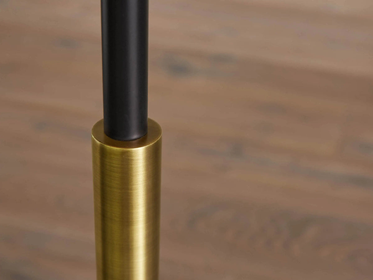 Ardea Floor Lamp with a matte black pole, antique brass detail, natural linen shade, and round brass base, against a neutral wall.