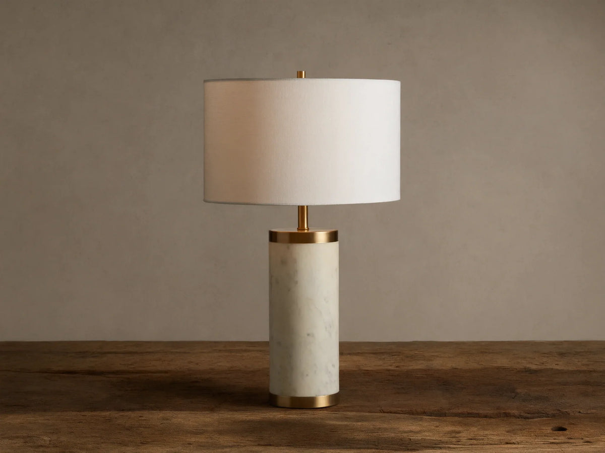 Caseti Table Lamp with ivory linen shade, cylindrical white marble base, and brass accents, on a wooden table.