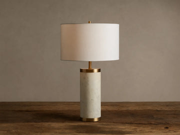 Caseti Table Lamp with ivory linen shade, cylindrical white marble base, and brass accents, on a wooden table.