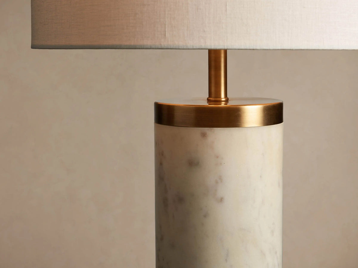 Caseti Table Lamp with ivory linen shade, cylindrical white marble base, and brass accents, on a wooden table.