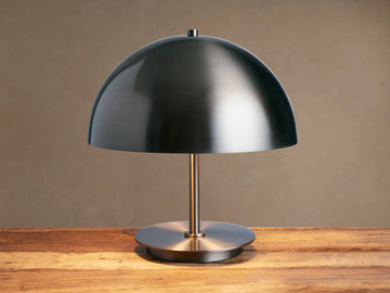 Malcom Table Lamp: dark brushed pewter dome shade, thin stem, and round base on a rustic wooden table.