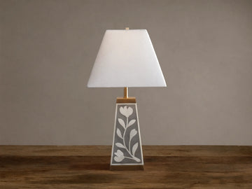 Divya Table Lamp with white fabric shade, gray base with white bone inlay floral motifs, brass trim, on wooden table.