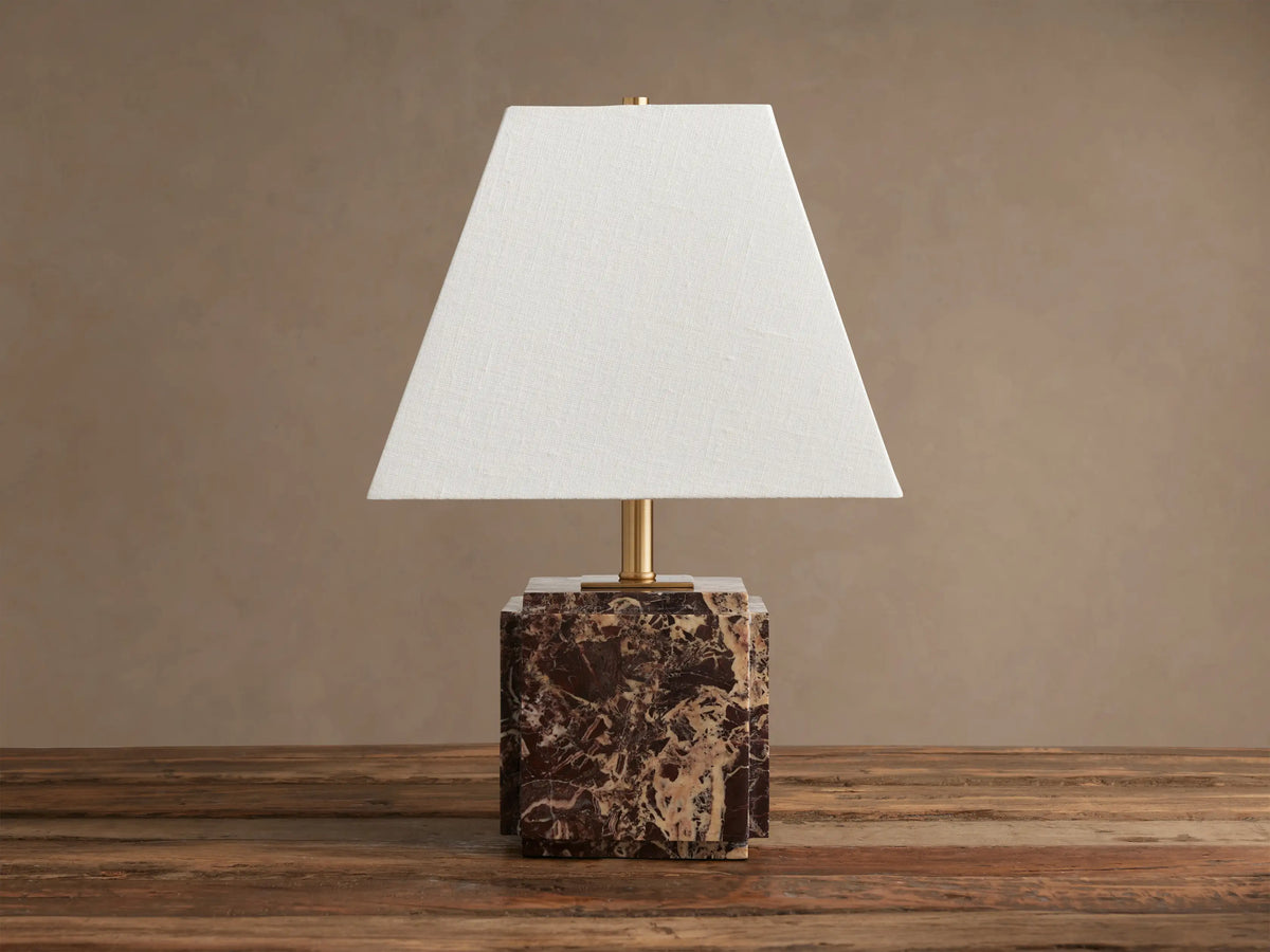 Fatima Table Lamp with a white tapered linen shade and a dark brown and white natural stone block base, on a wooden table.