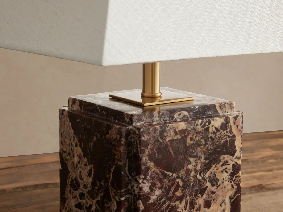 Fatima Table Lamp with dark brown veined natural stone cube base, gold stem, and tapered white linen shade on wooden table.