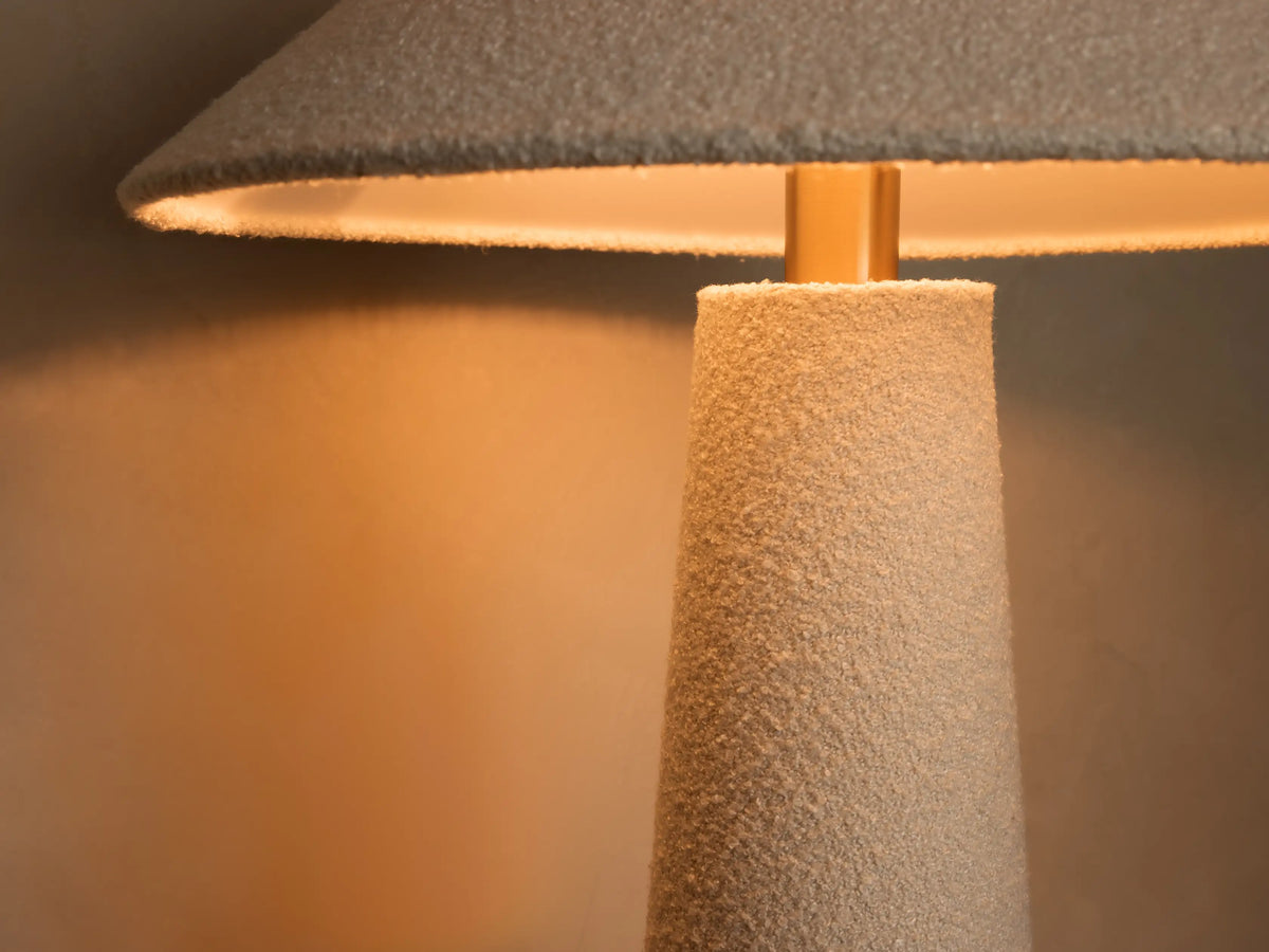 Close-up of a white bouclv©-textured base of a decorative object with a round wooden bottom on a wood table.