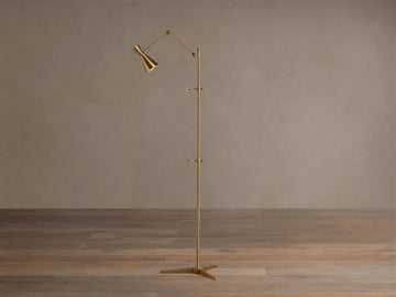 Tall, slender gold brass Jaxtyn Easel Floor Lamp with an angled light head, X-base, and small art display hooks.