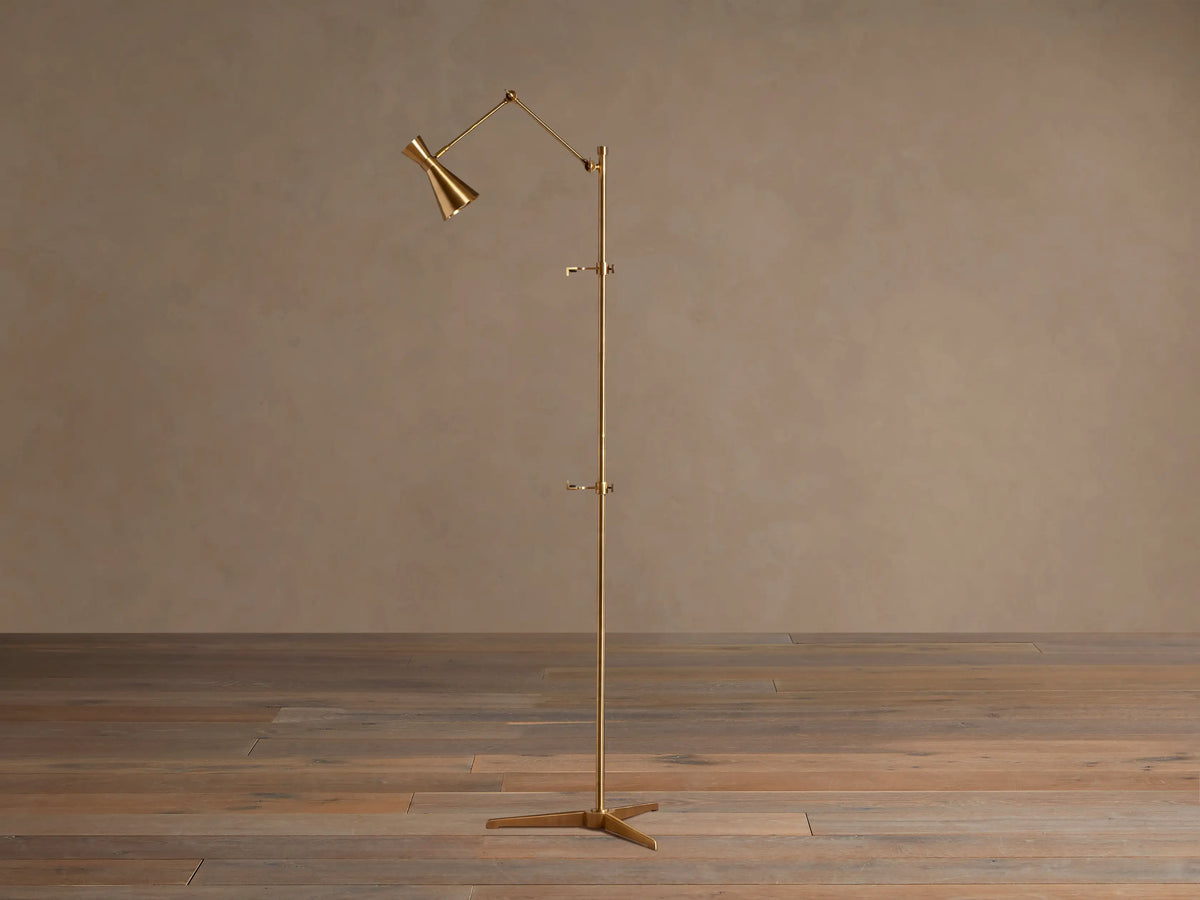Tall, slender gold brass Jaxtyn Easel Floor Lamp with an angled light head, X-base, and small art display hooks.