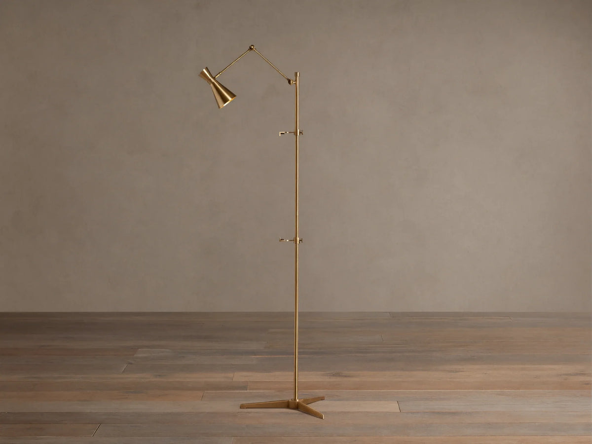Tall, slender gold brass Jaxtyn Easel Floor Lamp with an angled light head, X-base, and small art display hooks.