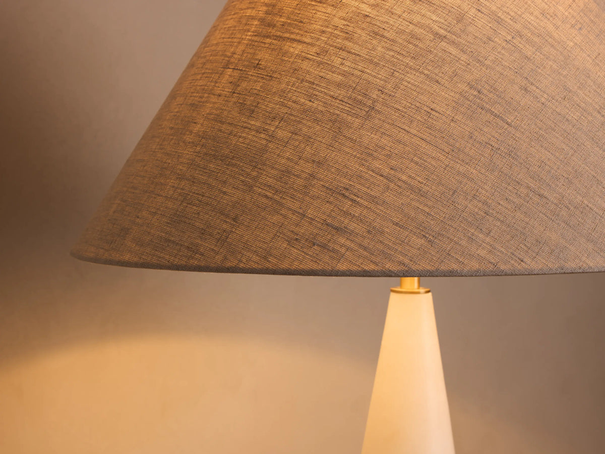 Front view of a white marble floor lamp with a beige conical shade, sculpted stem with brass accents, and round marble base.