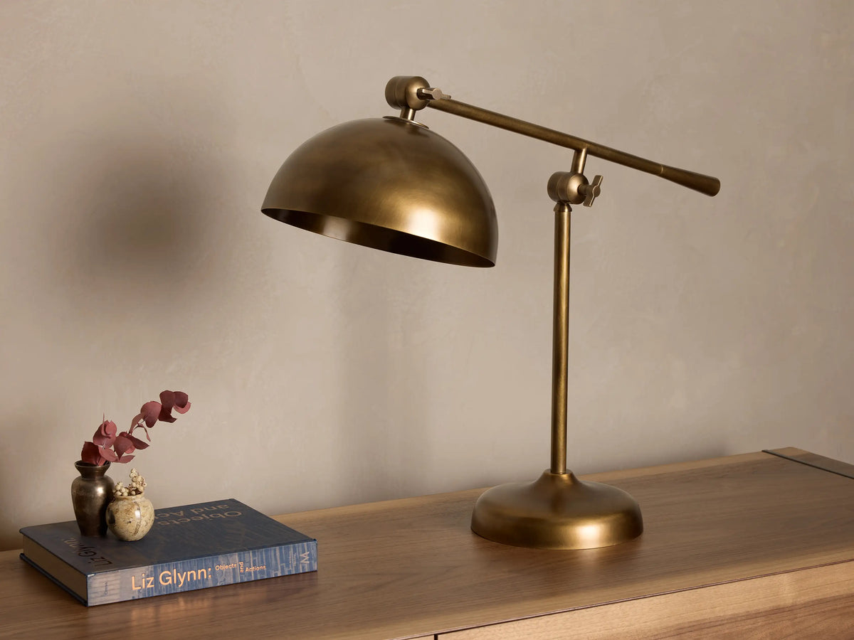 Front view of an antiqued brass industrial style desk lamp with an adjustable arm and dome shade, on a wooden surface.