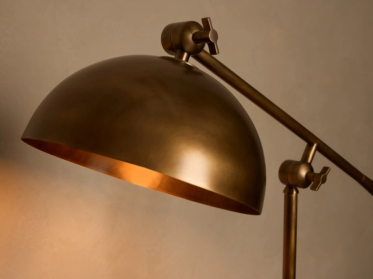 Front view of an illuminated brass industrial-style adjustable table lamp with a domed shade on a wooden surface.