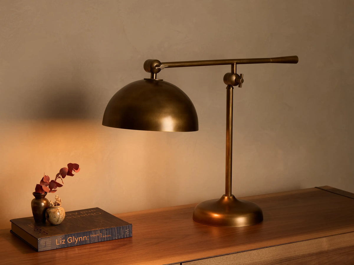 Close-up of antique brass dome lamp shade with warm, reflective interior. Features adjustable arm with knurled knobs.